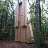 One side of a large wooden climbing tower that is completely perpendicular to the ground with two long wooden pieces that stick out further than the rest.