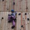 A young girl smiles as she makes her way up a wooden climbing tower.