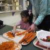 An adult helps a young girl peel carrots in a kitchen area.