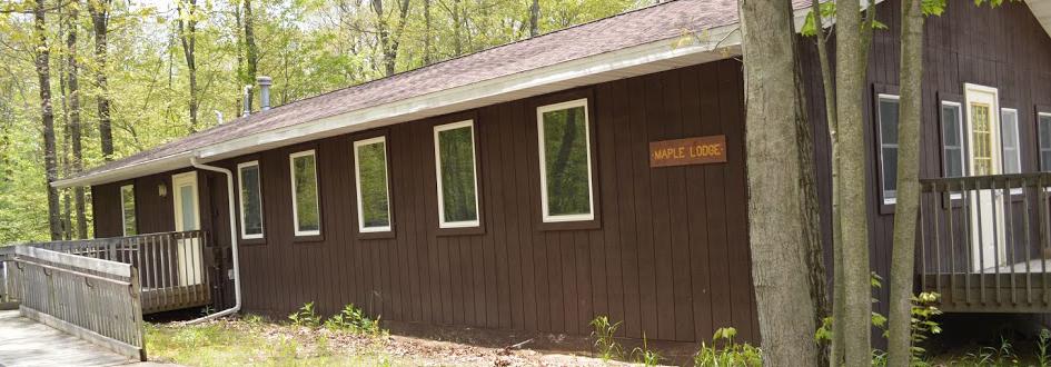 A brown rectangular building features a sign that says "Maple Lodge" and a ramp leading up to each door.