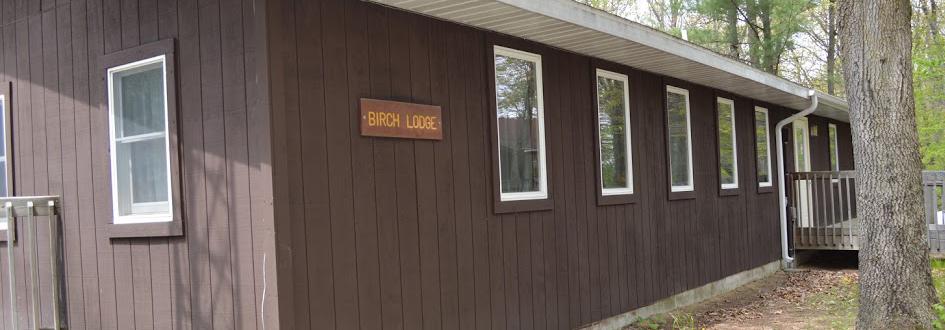 The side of a brown building with a sign on it that says "Birch Lodge."